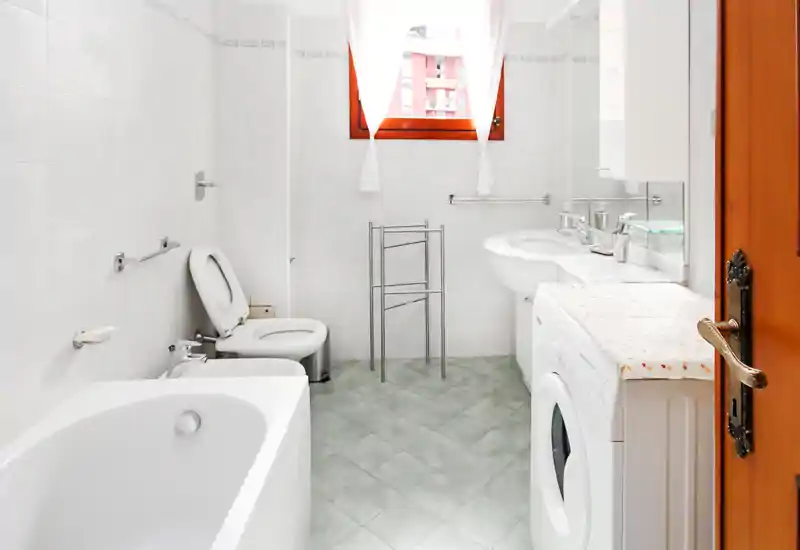 Baño luminoso y limpio con bañera, bidé, inodoro y lavabo; la ventana aporta luz natural y una apariencia moderna y ordenada.