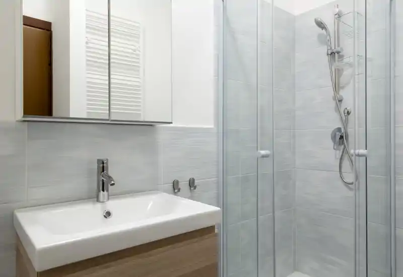 Bagno moderno e compatto con lavabo, mobile specchiato e doccia con pareti in vetro dotata di soffione a mano.