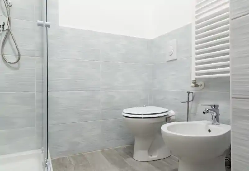 Bagno moderno e luminoso con wc, bidet, box doccia e piastrelle chiare; ambiente pulito e ben illuminato, perfetto per un annuncio.