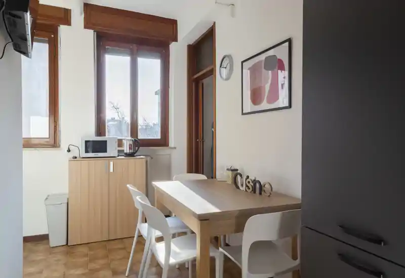 Accogliente angolo pranzo luminoso con tavolo in legno, quattro sedie bianche e grande finestra che illumina l'ambiente — perfetto per pasti informali.