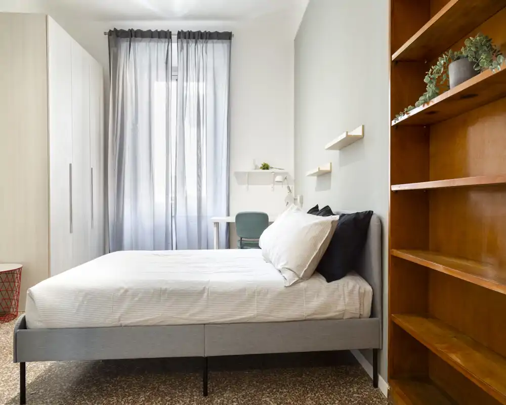 Dormitorio moderno y luminoso con cama doble bien hecha, ropa de cama clara, armario empotrado y un pequeño escritorio junto a la ventana — ideal para descansar y trabajar.