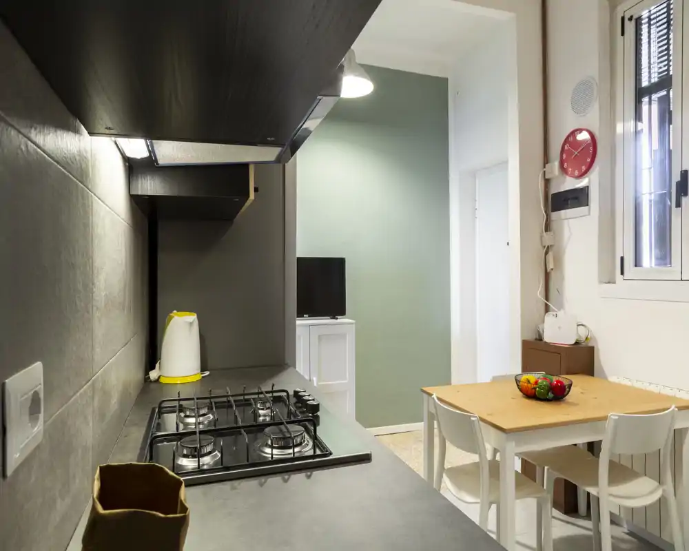 Cocina moderna compacta con placa de cuatro fuegos, hervidor y una pequeña mesa para cuatro — luminosa y ordenada, ideal para estancias en la ciudad.