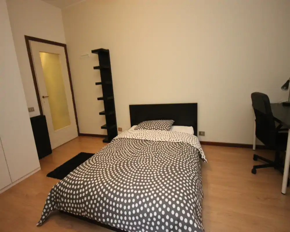 Camera singola ordinata con coperta a pois, testiera e una semplice scrivania; spazio luminoso e ordinato ideale per una persona sola.