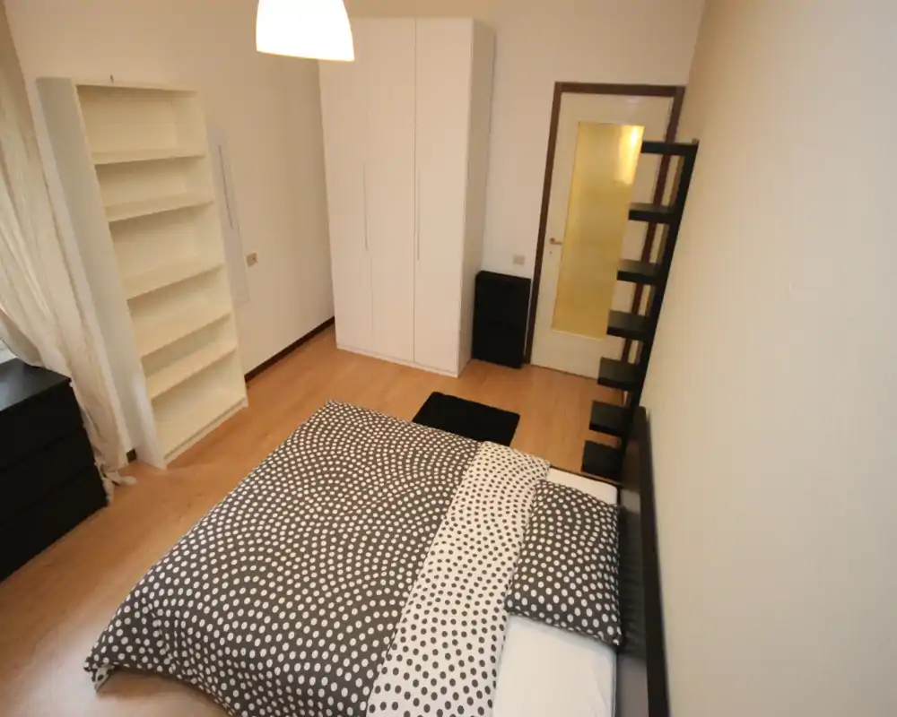 Camera da letto luminosa e ben arredata con copriletto a fantasia, armadio e scaffalatura; il letto è in primo piano e la stanza è pronta per gli ospiti.