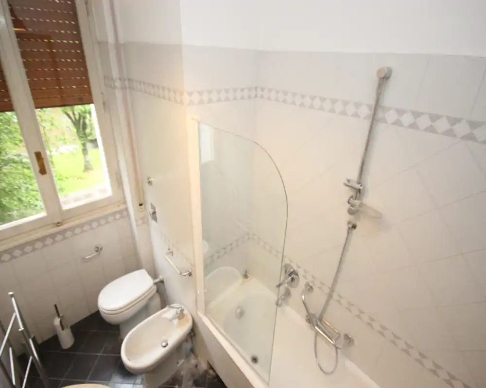 Bagno piastrellato luminoso con vasca e doccia, bidet e WC, dotato di finestra che assicura luce naturale.