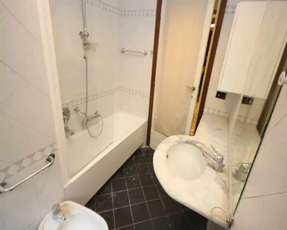 Bagno compatto con vasca-doccia, piano lavabo in marmo e pareti piastrellate. Layout efficiente per uno spazio ridotto e sanitari in ordine.