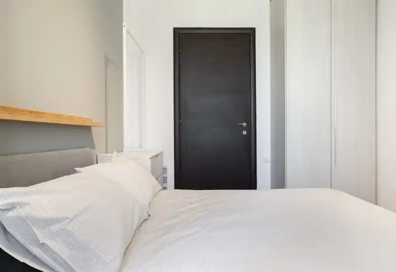 Dormitorio luminoso y minimalista con cama bien hecha, mesita y armario empotrado — ideal para anuncios que destaquen un estilo moderno y limpio.