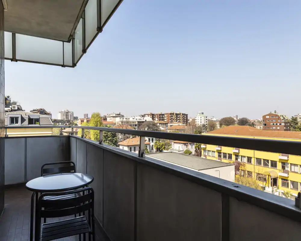 Sunny balcony with a small table and chairs and a clear city view — ideal for morning coffee or relaxing outdoors.