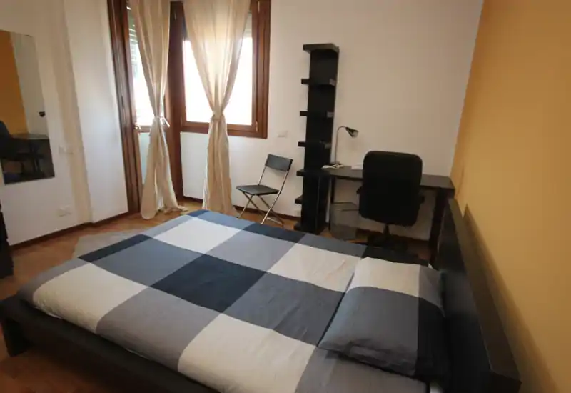 Bright, neatly staged bedroom with a large low platform bed, desk and natural light from a window. The room shows a tidy sleeping area ideal for rental listings.