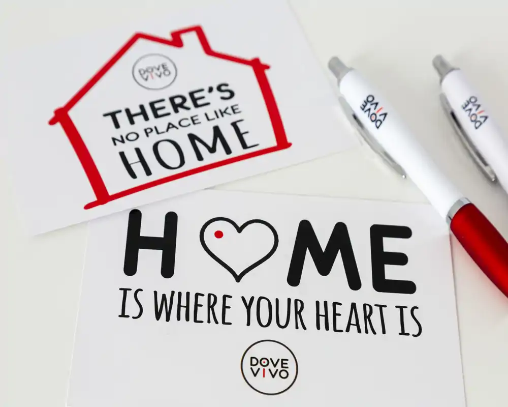 Close-up of printed cards and pens with the slogan "Home is where your heart is" on a clean surface; not a photo of an interior room.