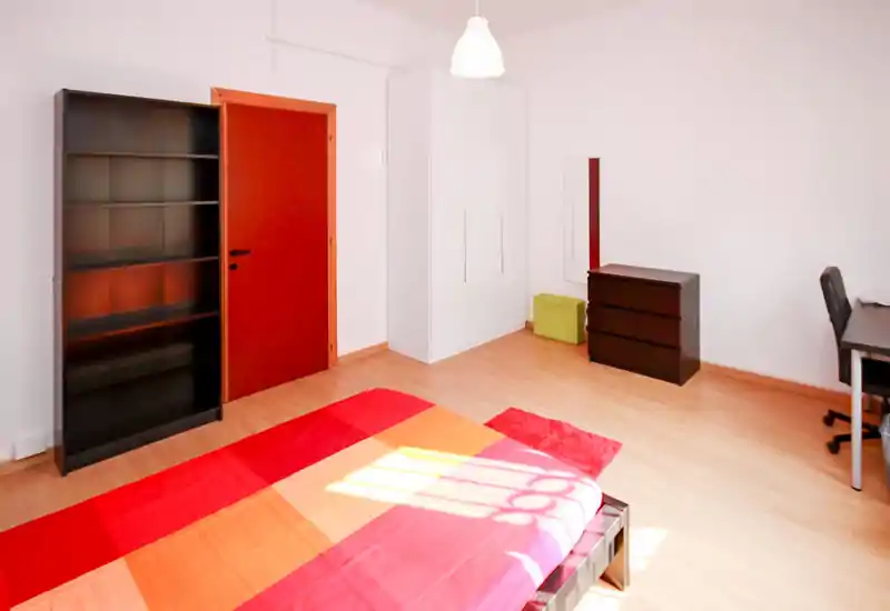 Spacious, bright bedroom with colorful bedding, a wardrobe, chest of drawers and a desk — ideal for a comfortable single or double stay.