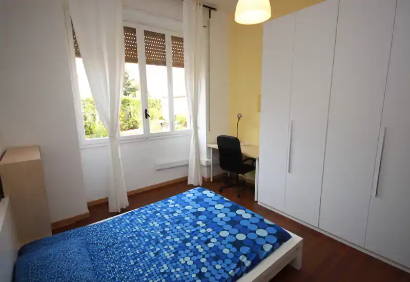 Camera da letto luminosa e ben arredata con letto matrimoniale, ampia armadiatura e scrivania vicino alla finestra. Luce naturale e colori caldi la rendono accogliente per soggiorni brevi o lunghi.