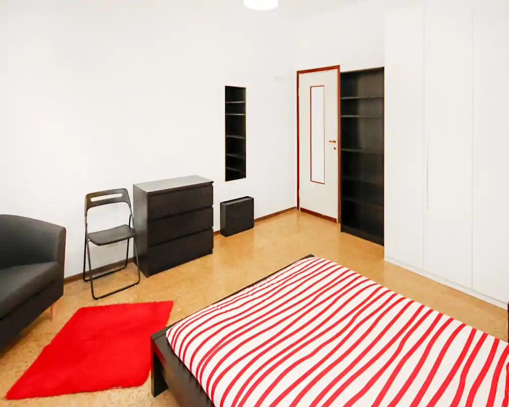 Dormitorio luminoso y minimalista con cama baja y edredón rojo y blanco a rayas, alfombra roja y muebles negros que crean un ambiente moderno y acogedor.