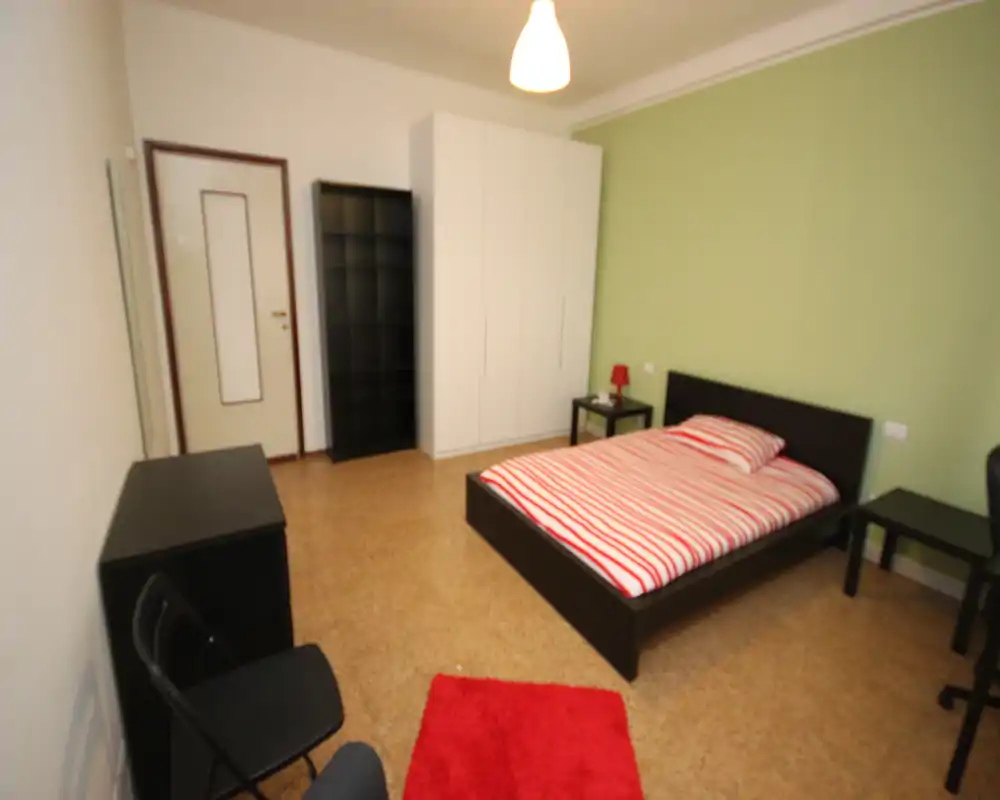 Dormitorio doble luminoso y ordenado con una cama baja de estructura oscura, ropa de cama a rayas y mesitas a juego; armario y estantería ofrecen buen almacenamiento.
