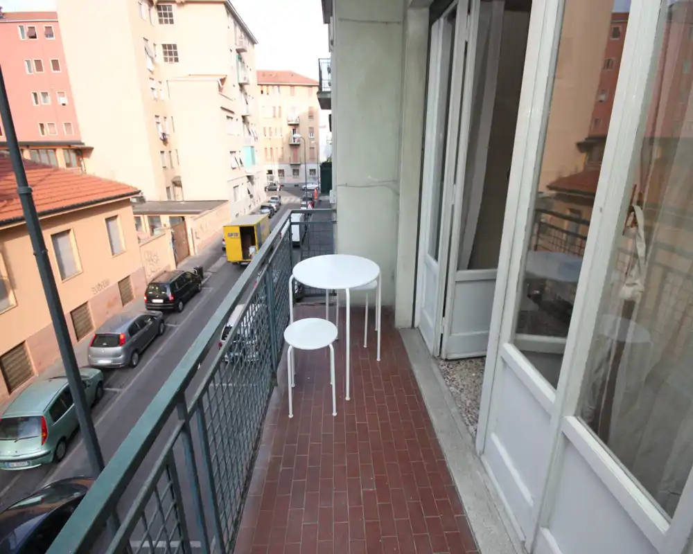 Narrow balcony with tiled floor, small white bistro table and stool, and view over a quiet street — ideal for morning coffee.