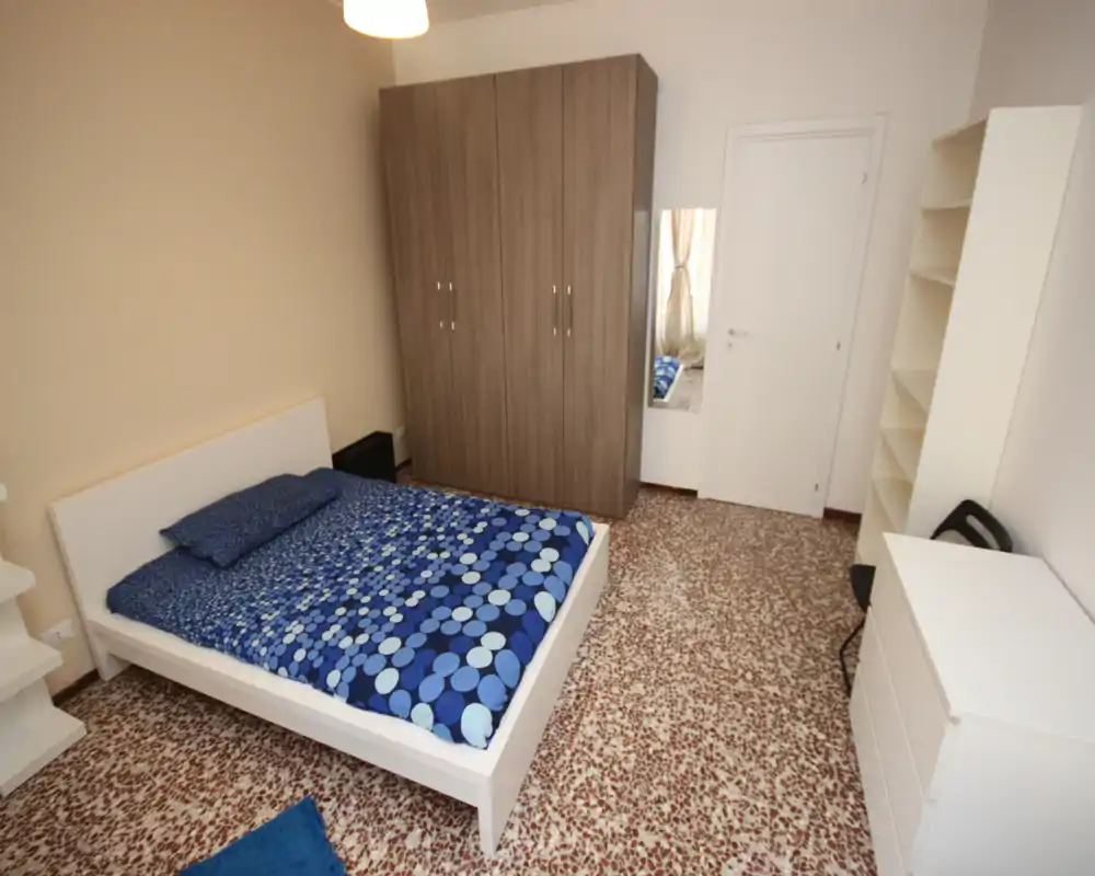 Bright, well-arranged bedroom with a double bed, large wardrobe and shelving; contemporary simple décor with blue patterned bedding.