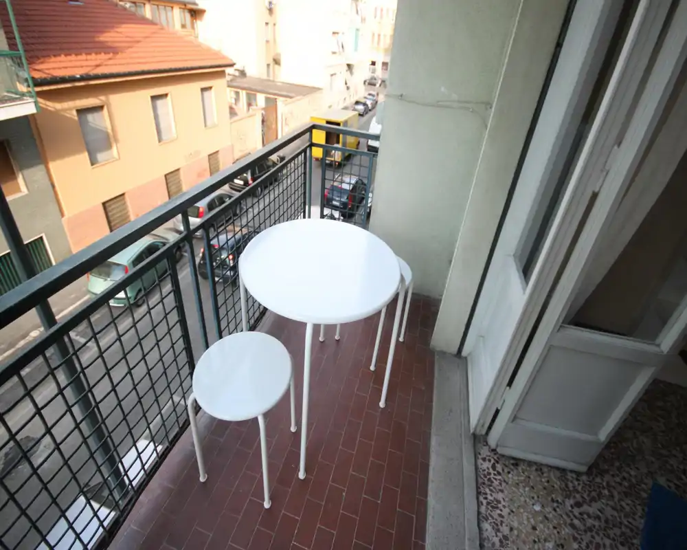 Small urban balcony with a round white table and two stools, overlooking a residential street. Ideal for a morning coffee or compact outdoor seating.