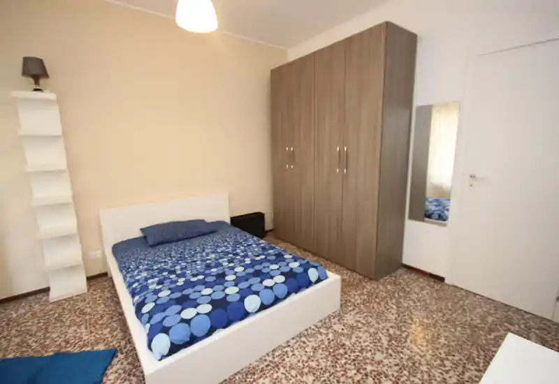 Dormitorio luminoso y ordenado con cama doble, edredón azul estampado, amplio armario y espejo de cuerpo entero: una habitación sencilla y cómoda, perfecta para estancias cortas.