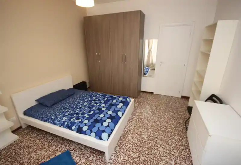 Dormitorio luminoso y bien organizado con cama doble, amplio armario y estanterías; decoración contemporánea y sencilla con ropa de cama azul estampada.