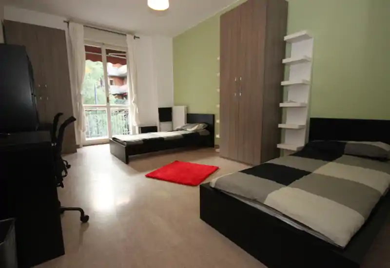 Grande chambre avec deux lits simples, balcon apportant une belle luminosité, placards et bureaux — moderne, épurée et idéale pour colocataires.