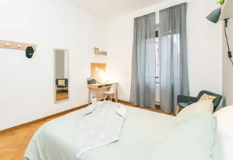 Dormitorio luminoso y acogedor con cama doble bien hecha, escritorio junto a la ventana y un sillón cómodo — ideal para descansar o trabajar.