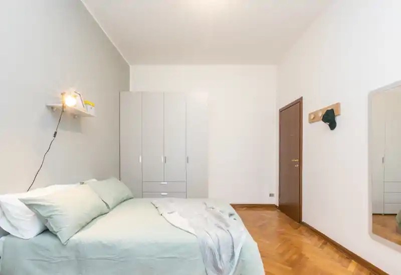 Dormitorio luminoso y bien presentado con cama doble arreglada, ropa de cama en tonos pastel y un amplio armario; suelo de parquet cálido.