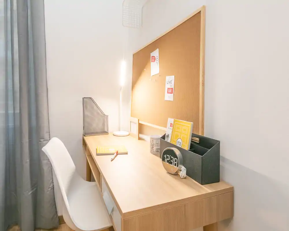 Espacio de trabajo en dormitorio ordenado con escritorio de madera, silla blanca, corcho y lámpara cálida — ideal para estudiar o trabajar desde casa.
