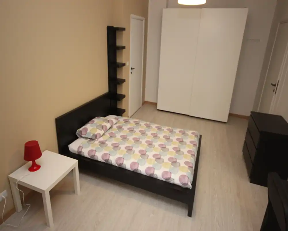 Camera da letto luminosa e arredata in modo essenziale con letto matrimoniale, comodino e armadio; toni neutri e linee pulite per un ambiente moderno e tranquillo.