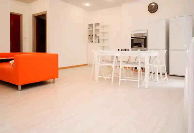 Bright, modern living area with a bold orange sofa and a white dining table set; minimalist, open-plan layout ideal for short-term stays.
