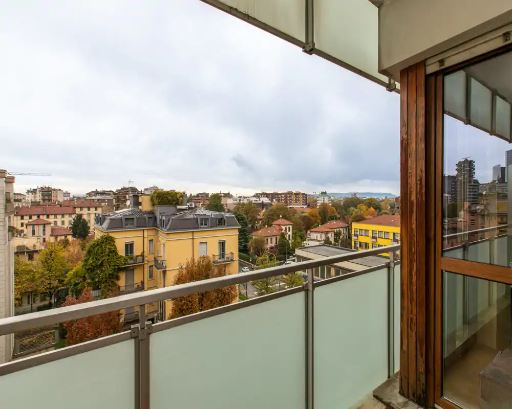 Sunny balcony with frosted glass railing and a wide city view — ideal for morning coffee with a view of tree-lined streets and colorful buildings.
