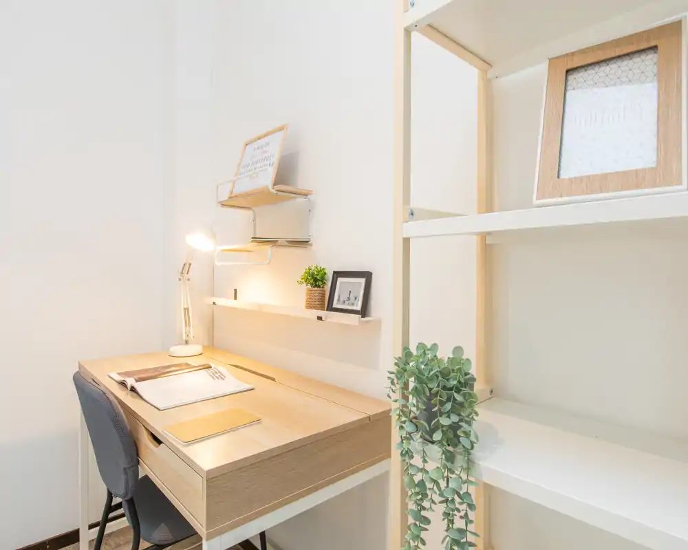 Bright, minimalist workspace corner with a wooden desk, desk lamp, chair and shelving—ideal for focused work or study.