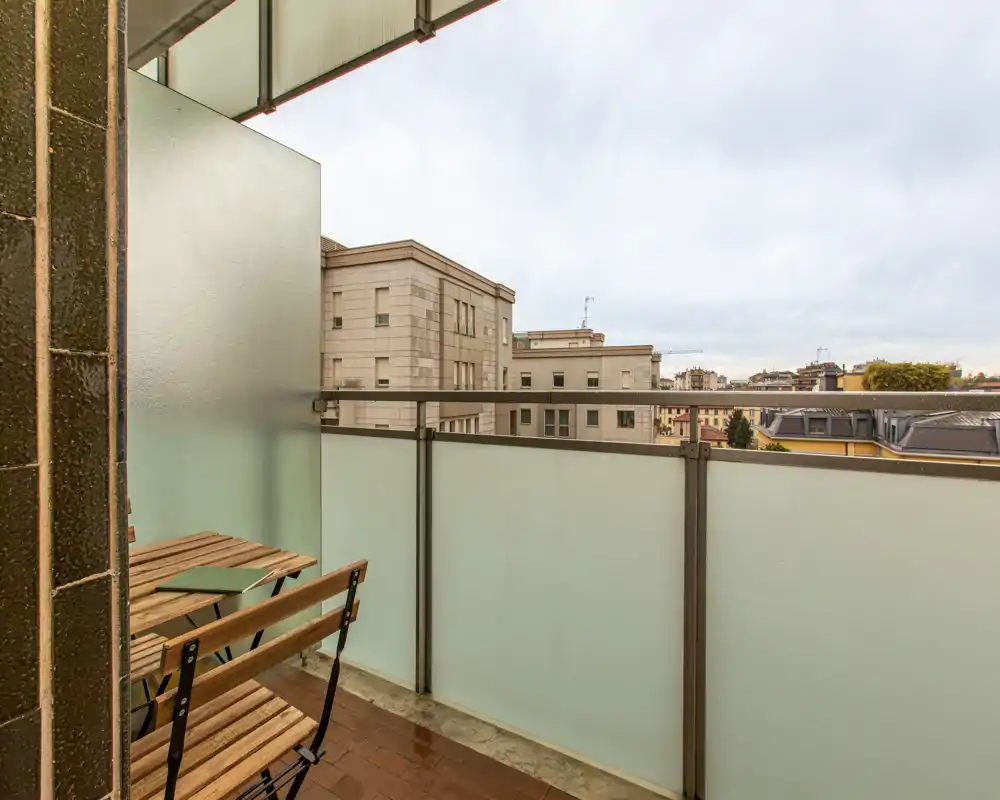 Small urban balcony with frosted glass privacy panels, metal railing and a compact wooden bistro table and chairs — ideal for morning coffee with a city view.