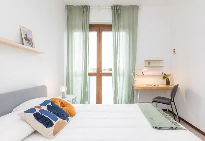 Dormitorio luminoso y con estilo, con cama doble cómoda, cojines decorativos y un pequeño escritorio junto a la ventana que deja entrar luz natural.