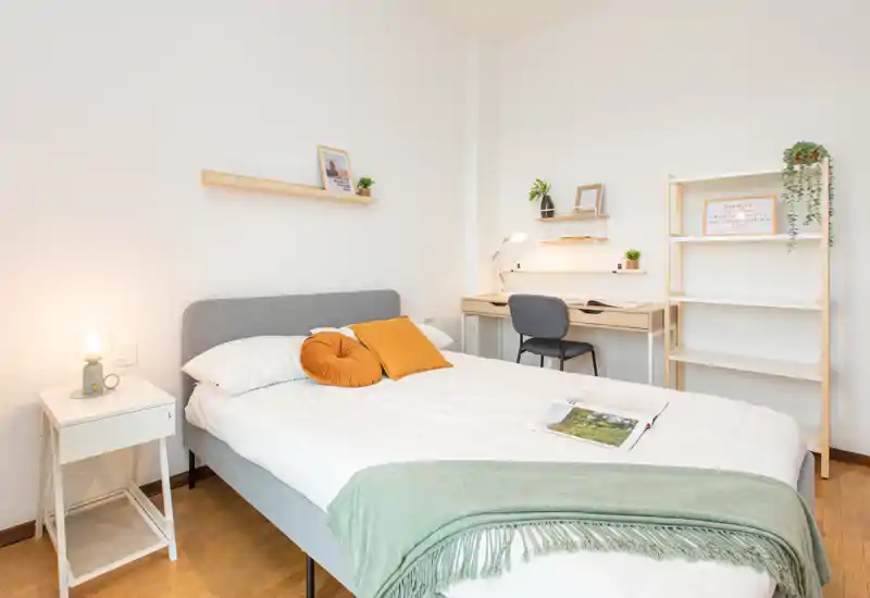 Camera da letto luminosa e ben arredata con letto matrimoniale ordinato, cuscini confortevoli e una piccola postazione di lavoro — ideale per rilassarsi o lavorare. Decorazioni neutre e illuminazione soffusa creano un'atmosfera tranquilla.
