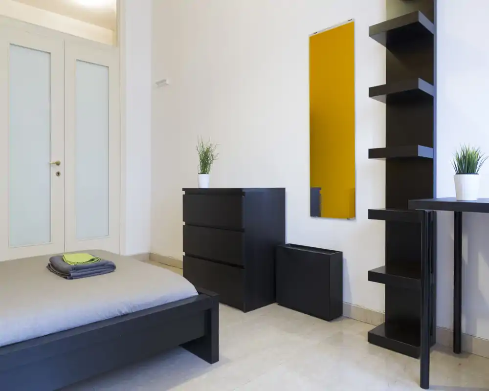 Camera da letto moderna e minimale con struttura del letto nera bassa, biancheria ordinata e mobili contenitori neri coordinati; luminosa, ordinata e perfetta per annunci.