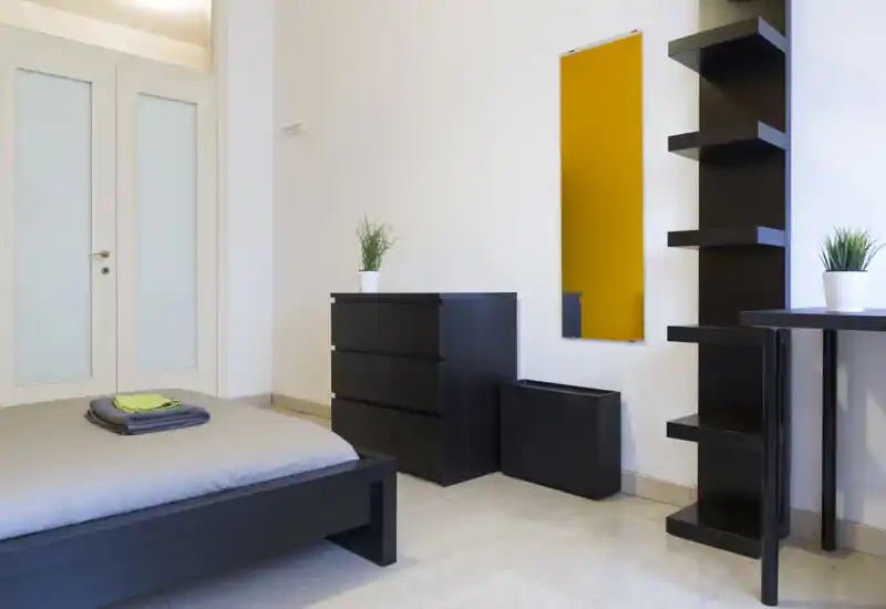 Camera da letto moderna e minimale con struttura del letto nera bassa, biancheria ordinata e mobili contenitori neri coordinati; luminosa, ordinata e perfetta per annunci.