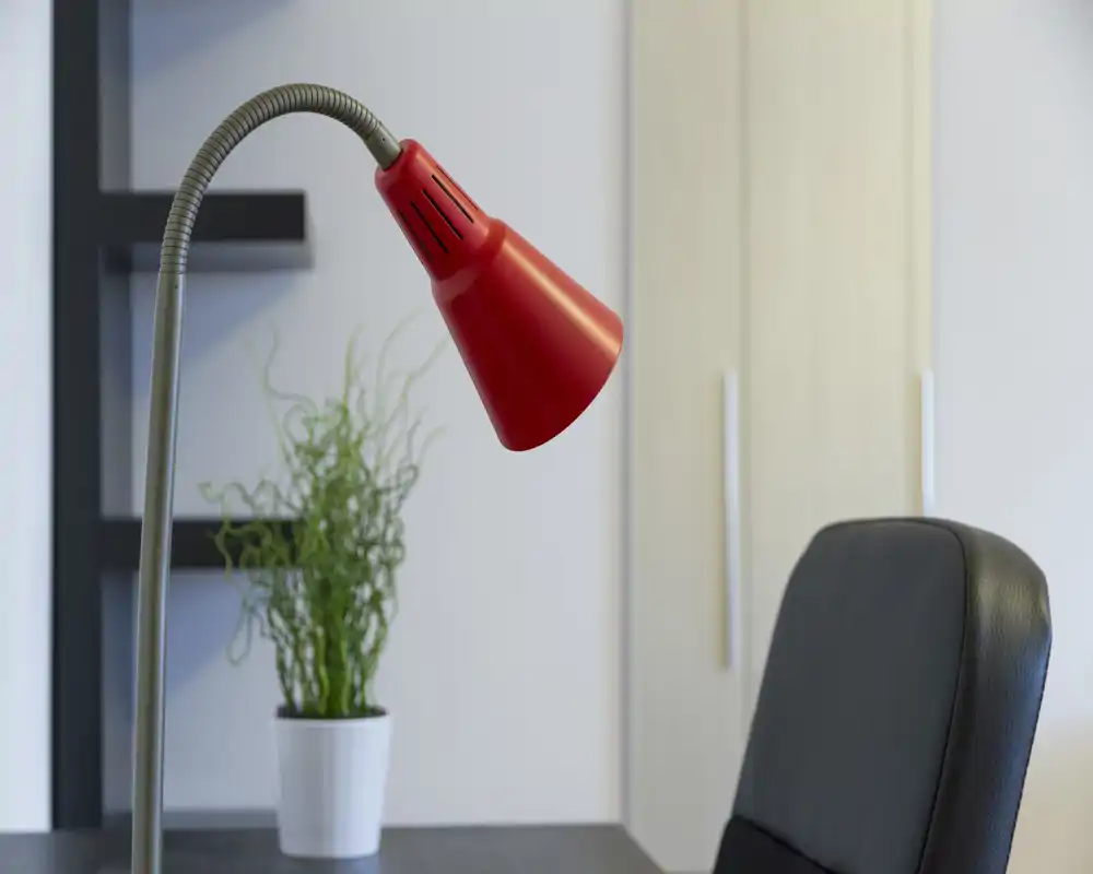 Angolo luminoso e moderno di un soggiorno/area lavoro con una lampada da tavolo rossa, una pianta in vaso e una sedia da ufficio: pulito, essenziale e ben illuminato.