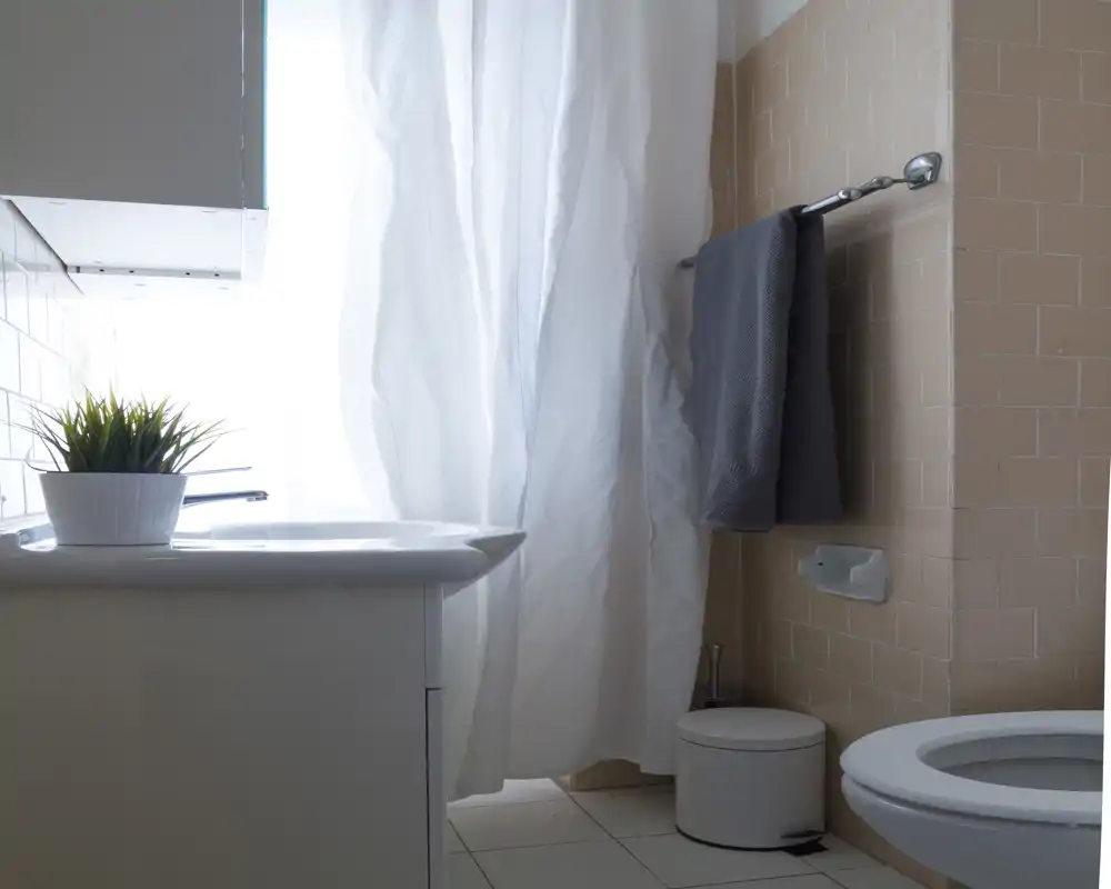Bagno pulito e luminoso con lavabo, WC, porta asciugamani e una tenda doccia chiara; la luce naturale filtra dalla finestra creando un'atmosfera fresca.