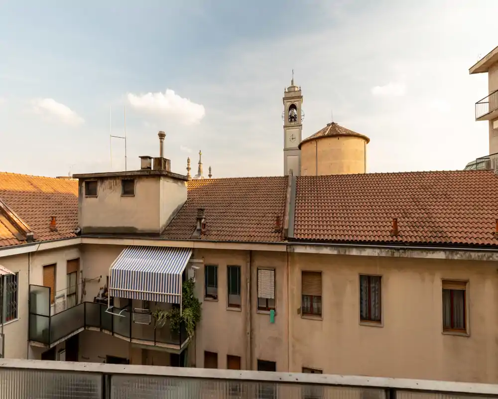 Vista tranquila desde un balcón con tejados de terracota y una torre de campanas cercana, con cálida luz de la tarde — ideal para un anuncio en el centro.