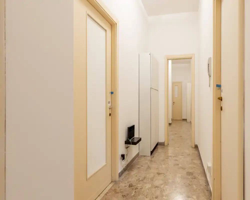 Pasillo/entrada limpio y bien iluminado con suelo de baldosas, varias puertas y disposición estrecha — apto como acceso de apartamento.
