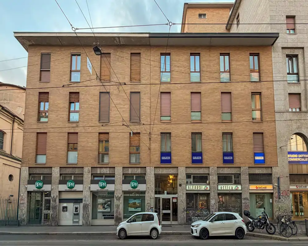Fachada que da a la calle con comercios en planta baja, coches aparcados y una vista clara del frente arquitectónico.
