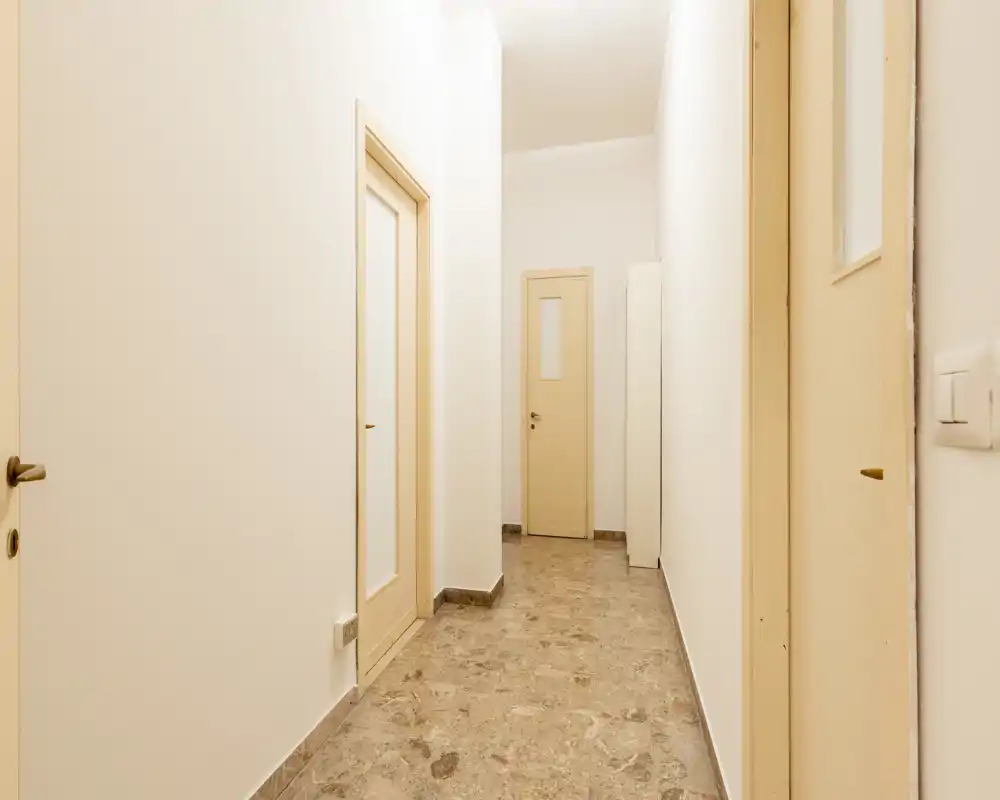 Pasillo estrecho y bien iluminado con suelo de piedra pulida y varias puertas interiores — ideal para mostrar la entrada y la zona de paso del piso.
