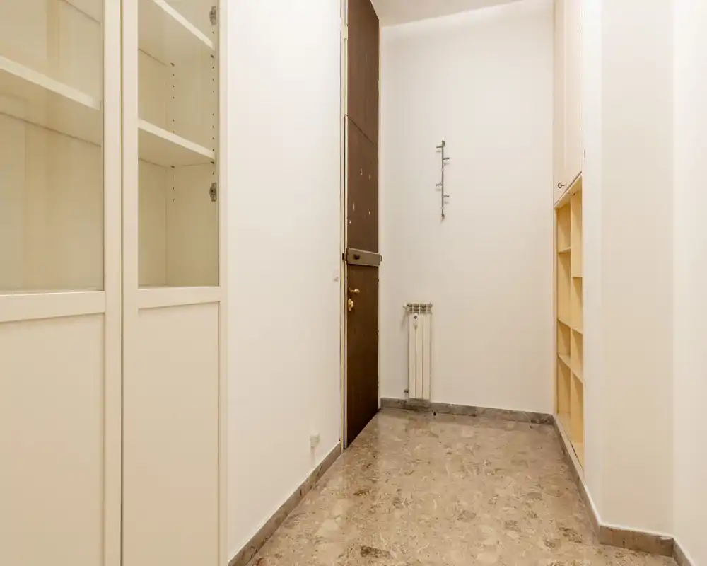 Entrada sencilla y bien iluminada con puerta de madera, perchas en la pared y estanterías empotradas — ideal para la entrada de un piso compacto.