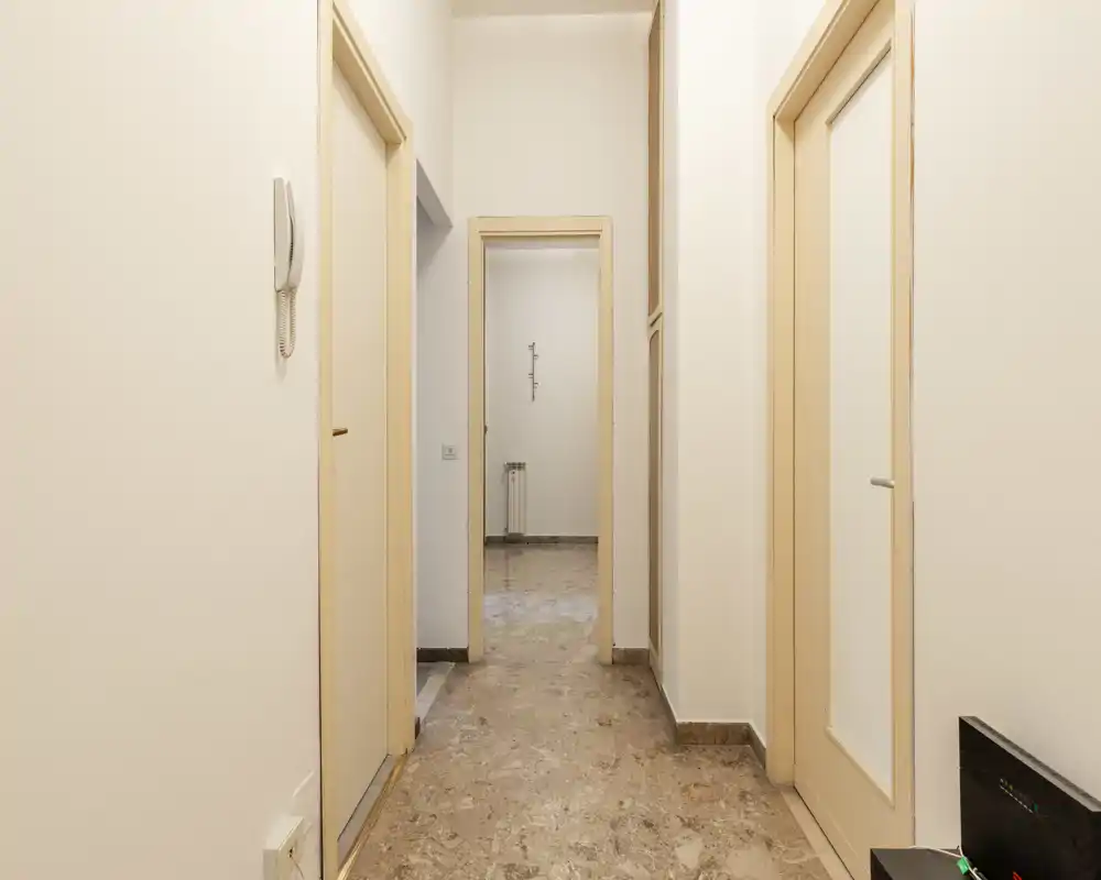 Entrada/pasillo del apartamento luminoso y limpio con paredes neutras, varias puertas y suelo efecto mármol — espacio de paso bien definido.