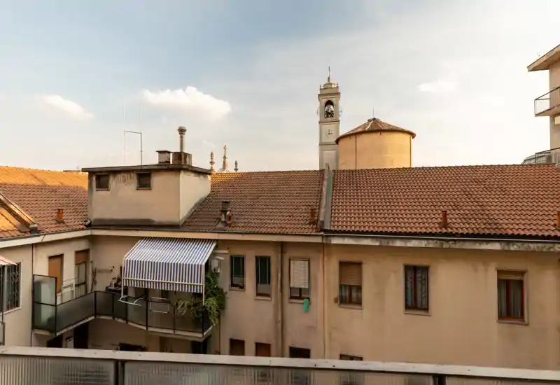 Quiet view from a balcony overlooking classic terracotta rooftops and a nearby bell tower, with warm afternoon light—ideal for a city-centre rental photo.
