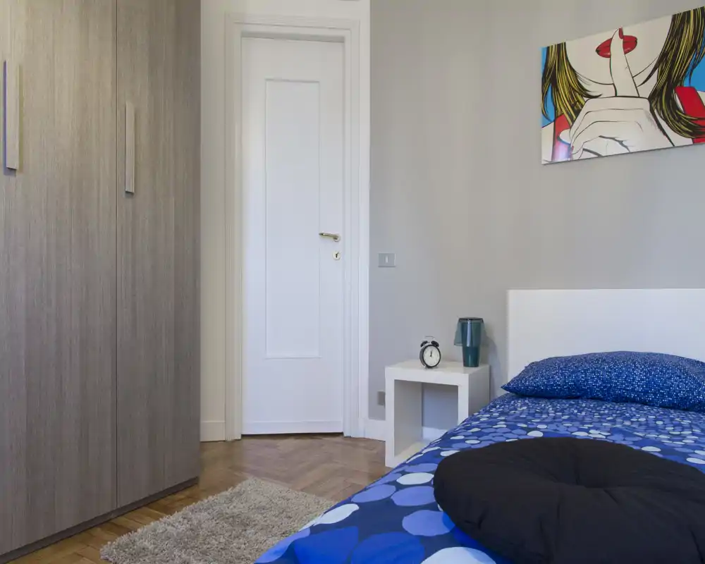 Dormitorio moderno y luminoso con ropa de cama azul estampada, mesita y armario — habitación individual/para invitados ordenada y bien iluminada, ideal para alquileres.