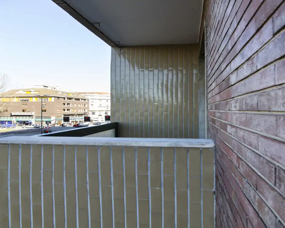 Pequeño balcón con antepecho alicatado y vista a la calle y edificios vecinos — luz diurna brillante y perspectiva urbana nítida.