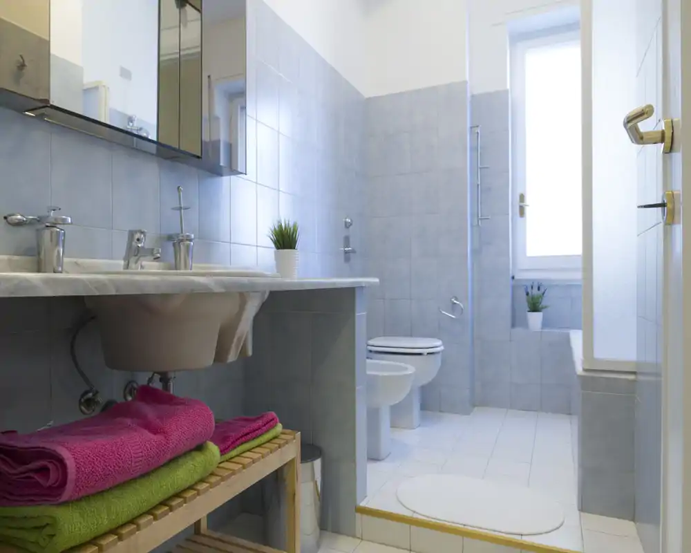 Baño luminoso y bien cuidado con doble lavabo, inodoro y bidé; azulejos azul claro y una ventana que aporta luz natural.