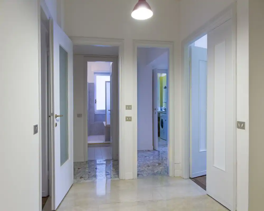 Vestíbulo luminoso y limpio con varias puertas que dan a otras estancias; suelo pulido y lámpara colgante sencilla crean una buena primera impresión.