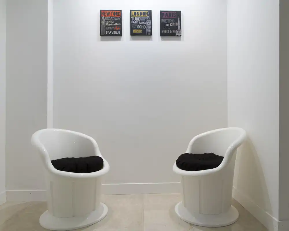 Pequeño recibidor o rincón de espera minimalista con dos sillones blancos modernos y cuadros en la pared; luminoso y despejado.
